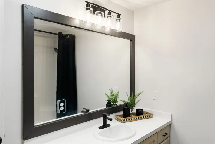 White countertop vanity with an undermount sink, a matte black faucet, and a large framed mirror