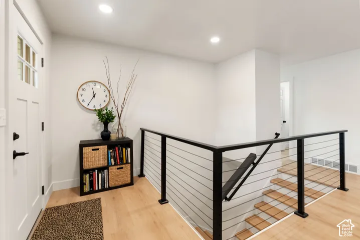 Modern cable railing system with a black finish, light wood-finish flooring, recessed lighting, and a paneled entry door with frosted glass