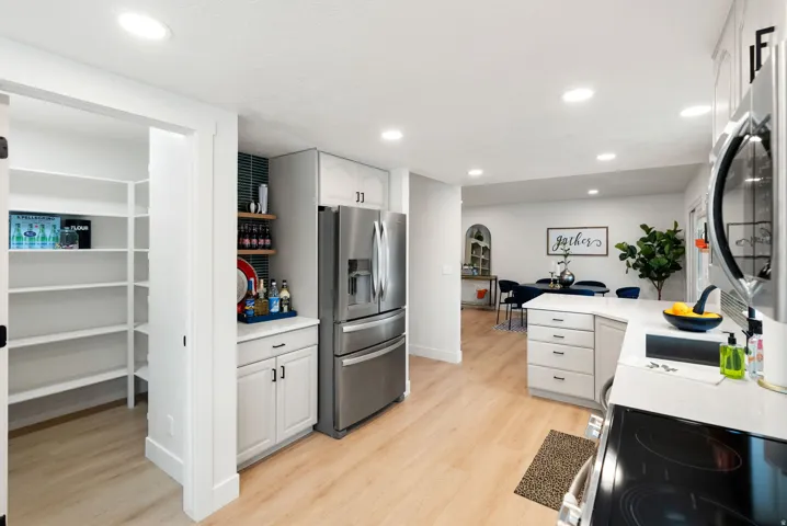 Well-appointed kitchen featuring light wood-finish flooring, recessed lighting, white cabinetry with dark hardware, and stainless steel appliances