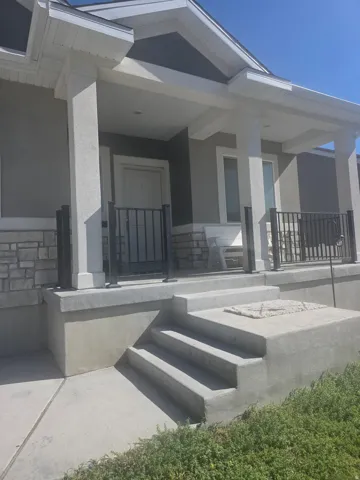 Front entry featuring a covered porch, stone veneer siding, concrete steps, and dark metal railings