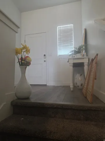 White paneled door, wood-finish flooring, white trim, and a window with blinds