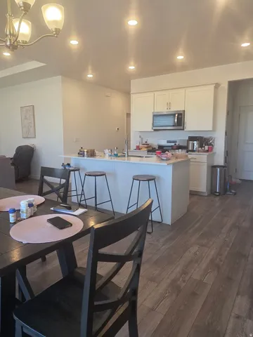 Kitchen featuring white cabinetry, stainless steel appliances, a white island with an integrated sink, and wood-finish flooring