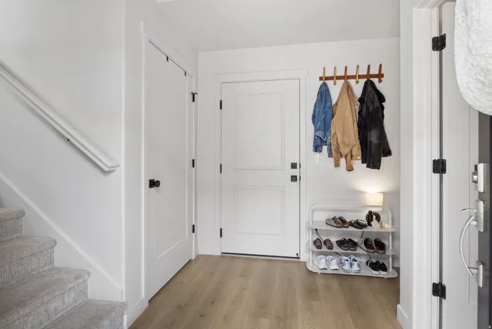 Bright entryway featuring hardwood flooring, white shaker-style doors with black hardware, and a wall-mounted wooden dowel rod with hooks for outerwear storage