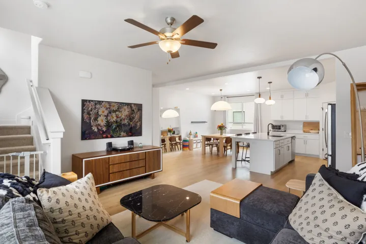 Open-concept living and dining area with wood-finish flooring, ceiling fan with integrated lighting, and stainless steel kitchen appliances