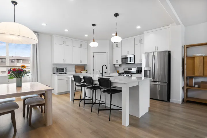 Open-concept kitchen with light wood-finish flooring, white cabinetry, a center island with seating, and stainless steel appliances