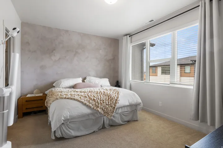 Bright secondary bedroom featuring neutral textured wall finishes, plush carpeting, and abundant natural light from dual windows with cellular shades