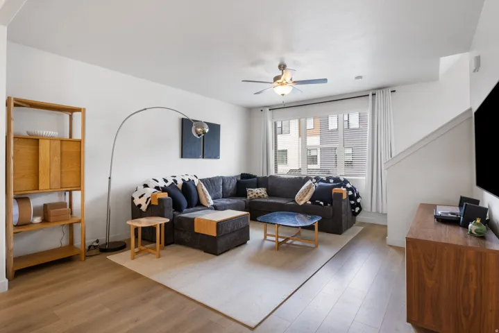 Light wood-finish flooring, white walls, and a ceiling fan with integrated lighting
