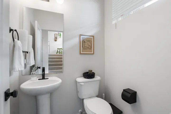 Pedestal sink with a matte black faucet, wall-mounted mirror, and white blinds