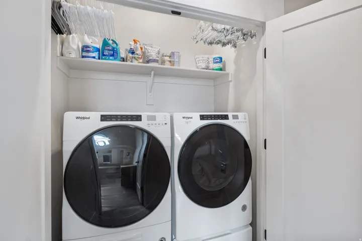 Dedicated laundry room featuring two front-load washers with large-capacity drums and digital controls, upper shelving for storage and supplies, and bright, clean finishes throughout