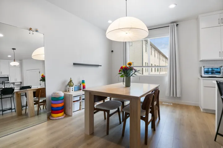 Open-concept dining area featuring wood-finish flooring, a contemporary pendant light fixture, recessed lighting, and a window with blinds