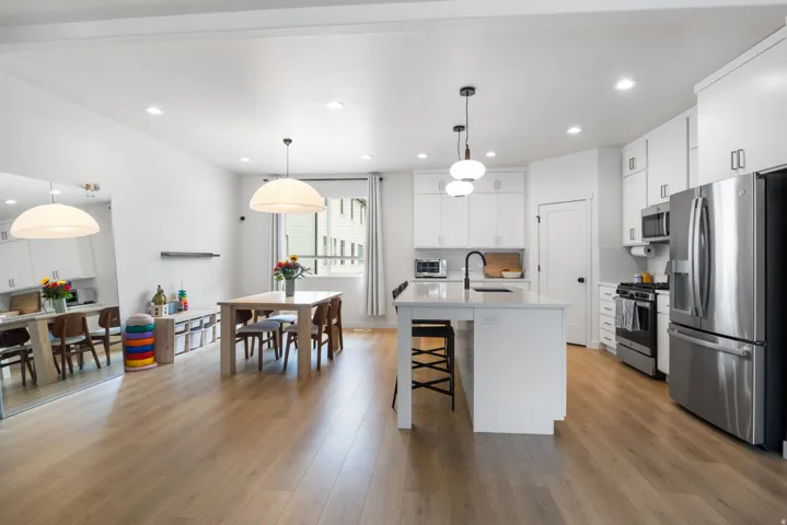 Open-concept kitchen and dining area featuring light-finish flooring, white cabinetry, a kitchen island with pendant lighting, and stainless steel appliances