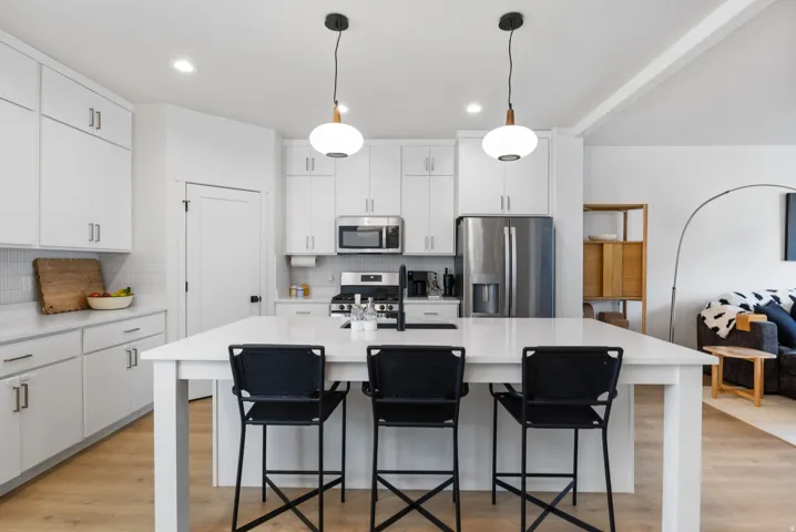 Modern kitchen featuring white cabinetry, a large center island with countertop seating, stainless steel appliances, and wood-finish flooring