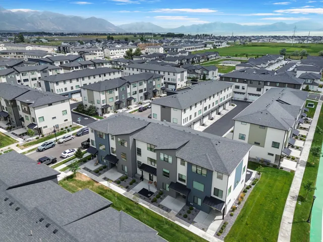 Modern residential community featuring contemporary townhome and multi-family architecture with clean-lined facades, mixed exterior finishes in charcoal and light tones, manicured landscaping with mature greenspace, and ample surface parking