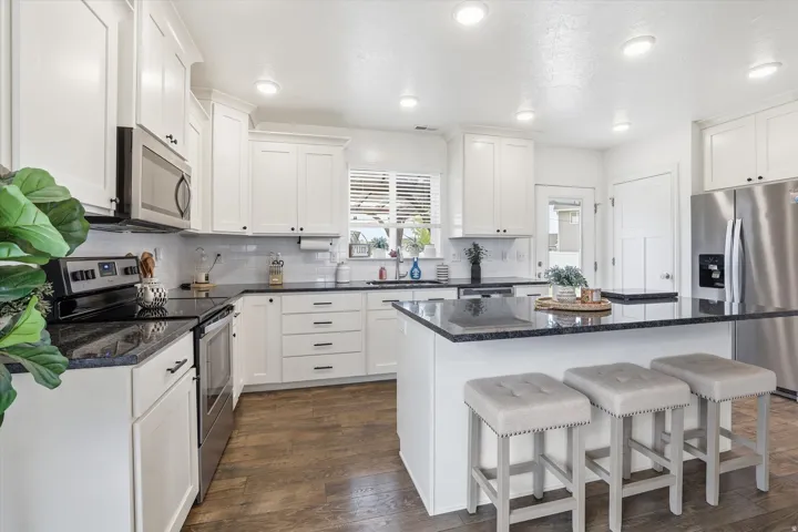 Kitchen featuring white shaker cabinetry, dark countertops, a large island with seating, stainless steel appliances, and wood-finish flooring