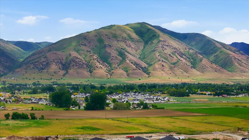 Scenic valley property featuring expansive agricultural land, mature tree-lined grounds, and dramatic mountain backdrop with multi-colored geological formations