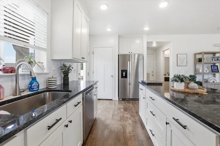White shaker cabinetry with dark hardware, stainless steel appliances, dark stone countertops, wood-finish flooring, and recessed lighting