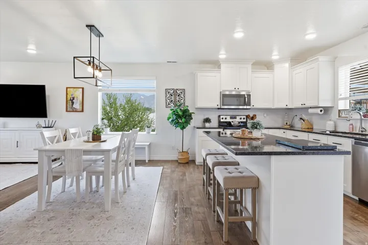 Open-concept living space featuring wood-finish flooring, white cabinetry, dark countertops, stainless steel appliances, and recessed lighting