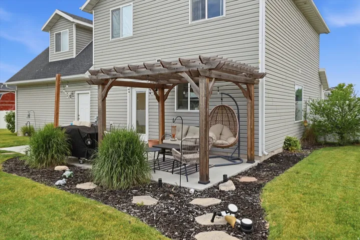 Backyard oasis featuring a wood-frame pergola with integrated seating area, decorative stone pathway, ornamental grasses, and mature landscaping with dark mulch beds