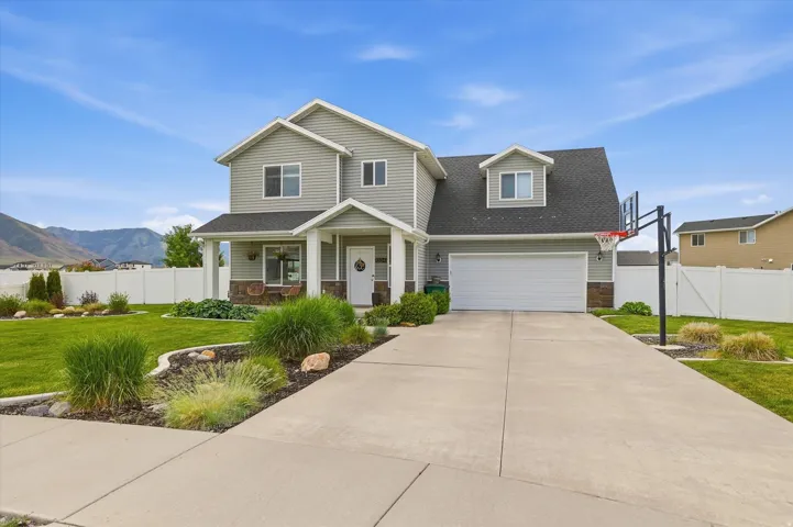 Two-story exterior with light gray siding, a covered porch with stone accents, a two-car garage, and a concrete driveway