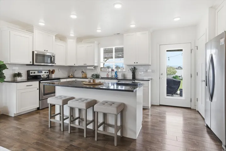 White cabinetry, dark stone countertops, stainless steel appliances, wood-finish flooring, and recessed lighting