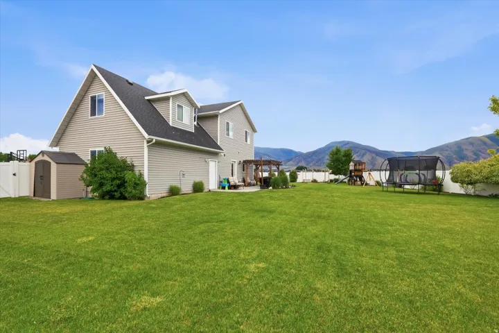 Expansive backyard featuring a manicured lawn, white privacy fencing, and a permanent storage shed