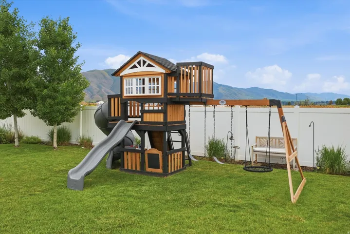 Expansive lawn with a white privacy fence, mature trees, and mountainous scenery