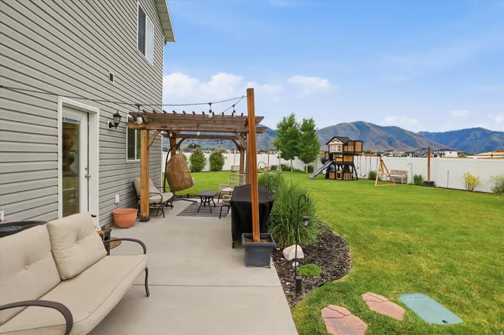 Expansive backyard featuring a concrete patio with a wood pergola, manicured lawn, and a white privacy fence