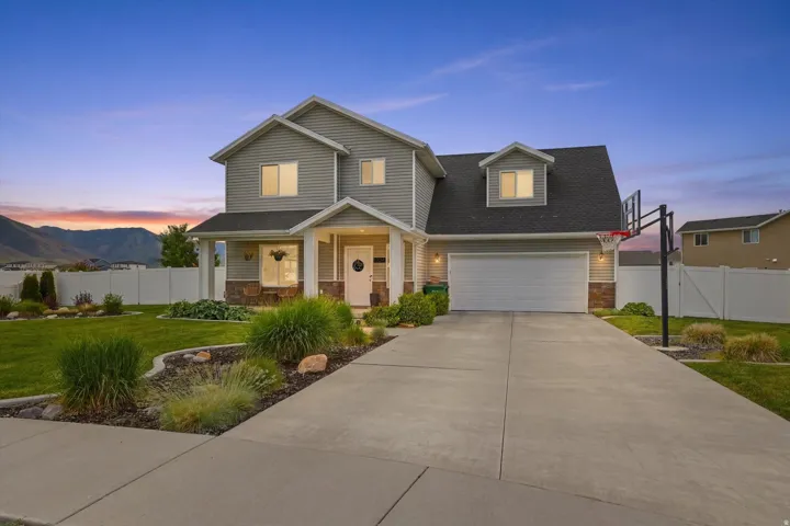 Two-story exterior with light gray siding, stone accents, a covered front porch, and an attached two-car garage
