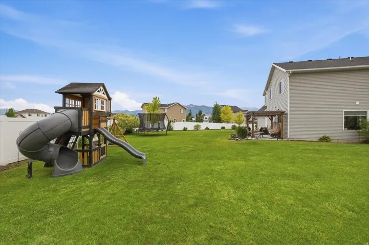 Expansive green lawn, white perimeter fencing, concrete patio area, and a wood pergola
