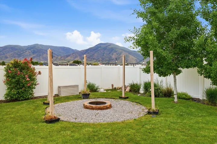 Expansive backyard featuring a manicured lawn, established trees, and a gravel fire pit area with a stone surround