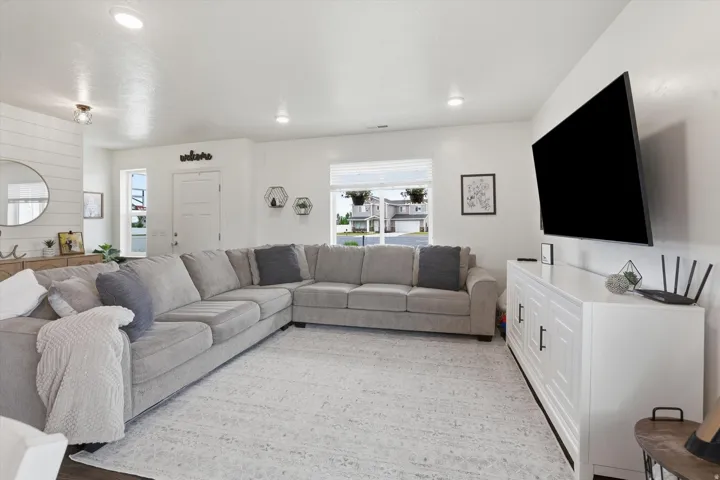 Bright, open-concept living space with recessed lighting, wood-finish flooring, and a white built-in media console