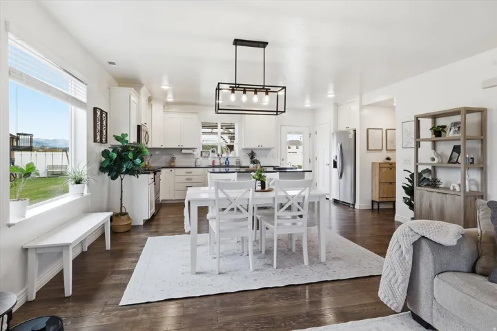 Hardwood-finish flooring, white cabinetry, dark countertops, stainless steel appliances, and a rectangular black-frame chandelier