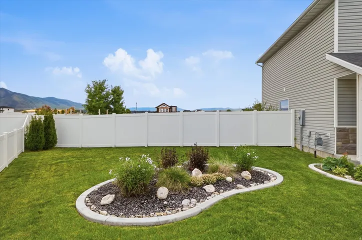 Expansive lawn with a white privacy fence, stone-edged landscaped beds, and a mountain backdrop