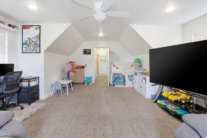 Carpeted room featuring a ceiling fan, recessed lighting, white walls, and an angled ceiling design
