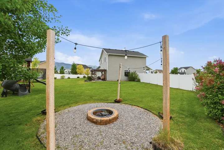 Expansive backyard featuring a stone fire pit, gravel patio, string lighting, and a manicured lawn