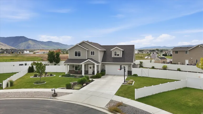 Two-story residence featuring a covered front porch, attached garage, concrete driveway, and white privacy fencing
