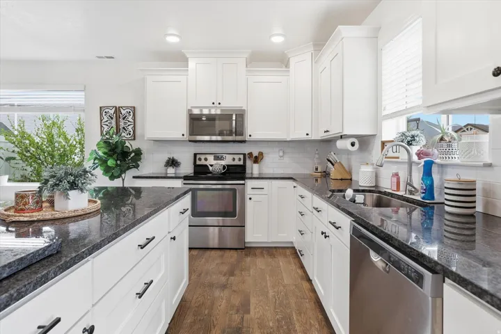Spacious kitchen with white cabinetry, dark stone countertops, stainless steel appliances, and wood-finish flooring