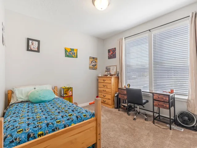 Carpeted room featuring a light wood bed frame, two windows with blinds and drapes, and a ceiling-mounted light fixture
