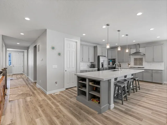 Contemporary kitchen featuring an oversized island with integrated shelving, pendant lighting, stainless steel appliances, a tile backsplash with a decorative accent, and abundant cabinet storage