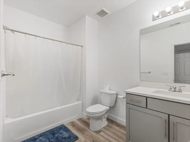 Full bathroom featuring a white tub-shower combination, a vanity with a light gray cabinet, a white countertop, and wood-finish flooring