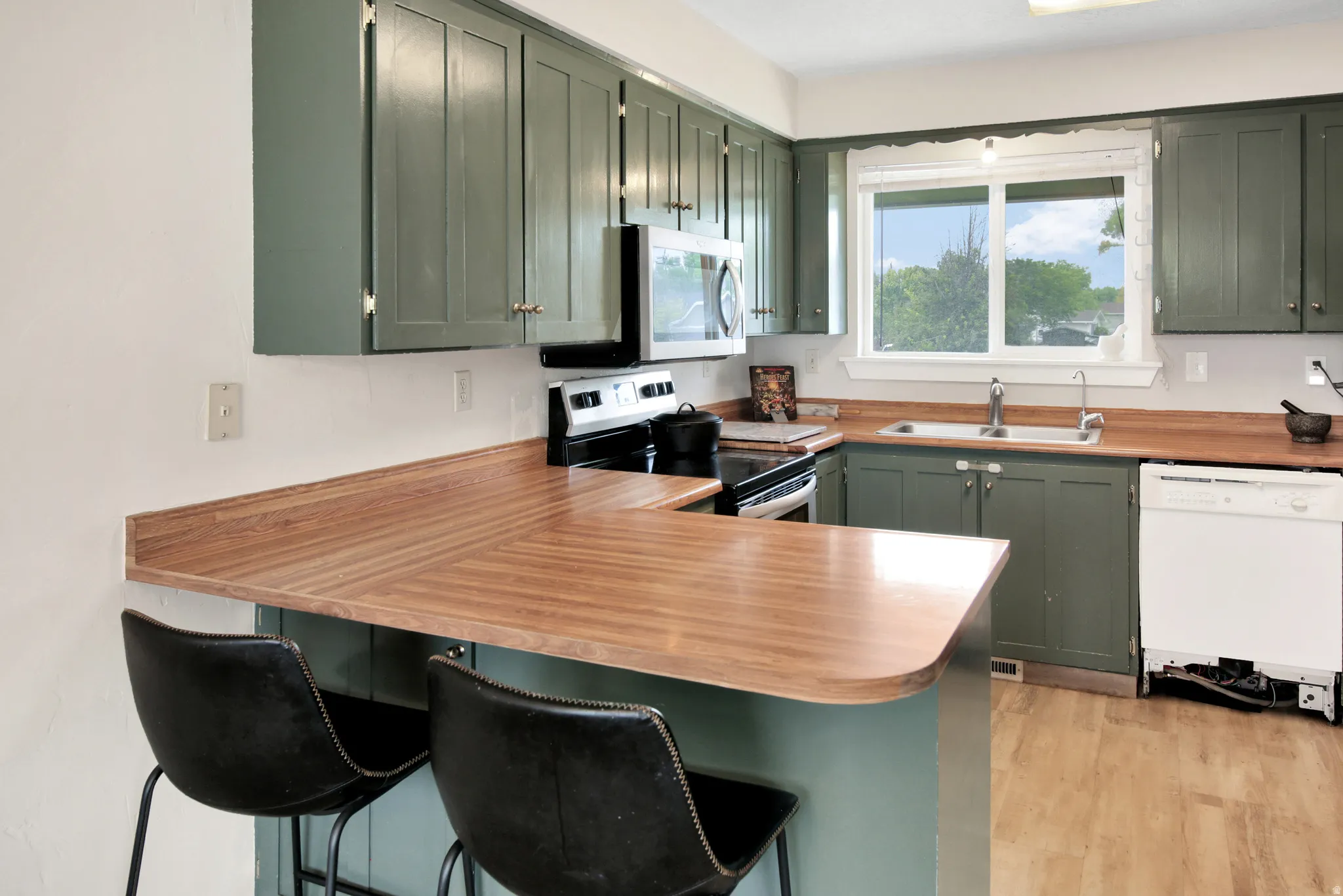 Kitchen with green cabinetry, wood-finish countertops, stainless steel microwave, black electric range, and wood-finish flooring