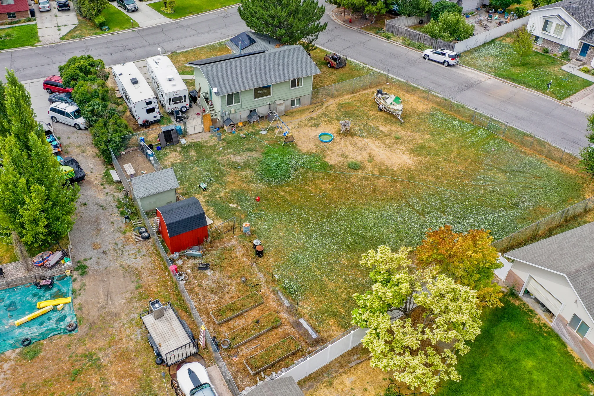 Expansive fenced yard with mature trees, established garden beds, and two storage sheds