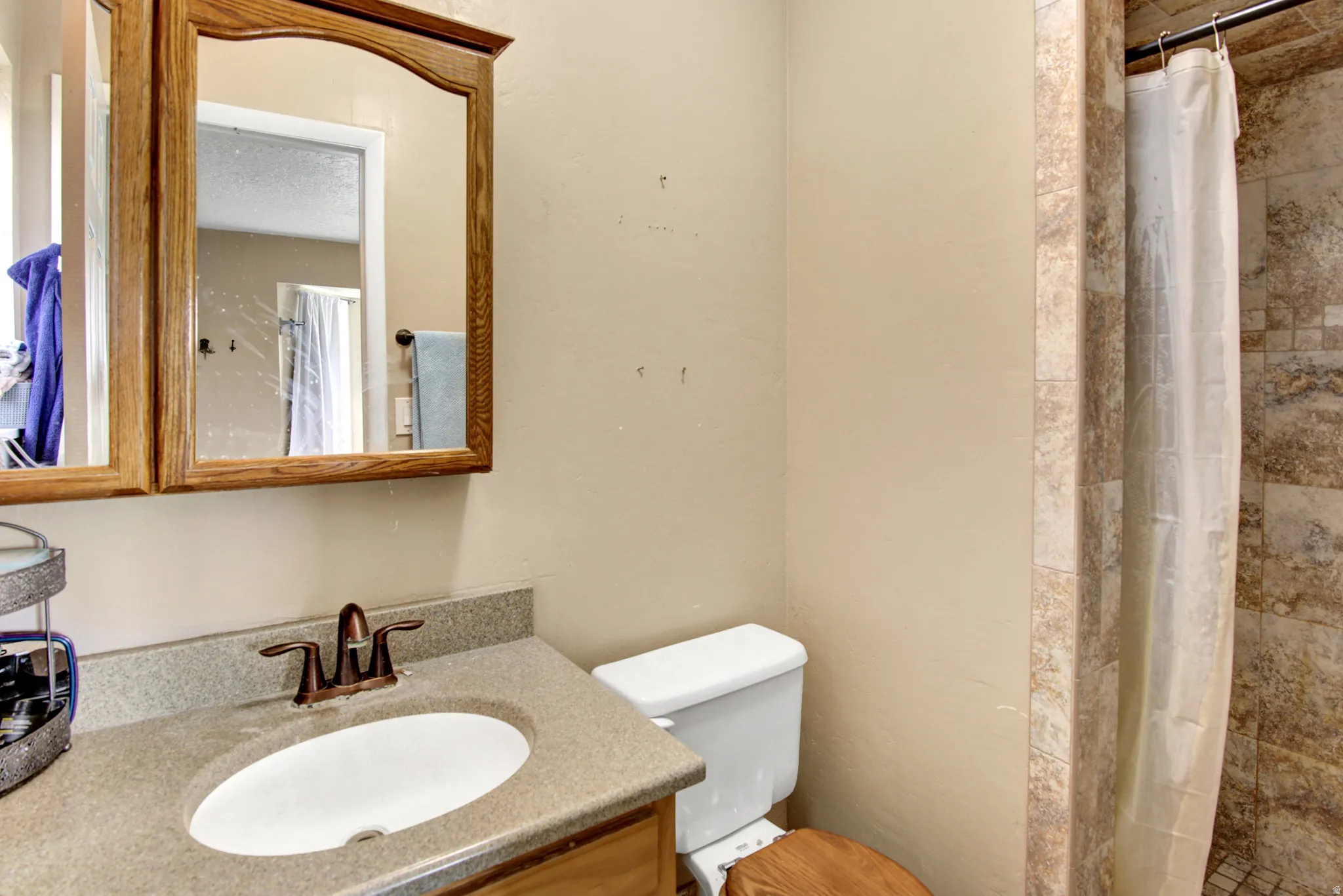 Vanity with integrated sink and bronze-finish faucet, framed medicine cabinet, toilet, and tiled shower surround