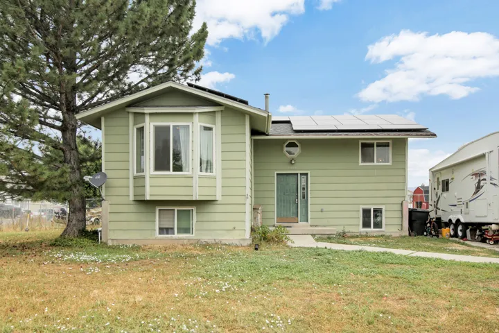 Light green siding exterior, bay window, front entry door, solar panels, and mature landscaping