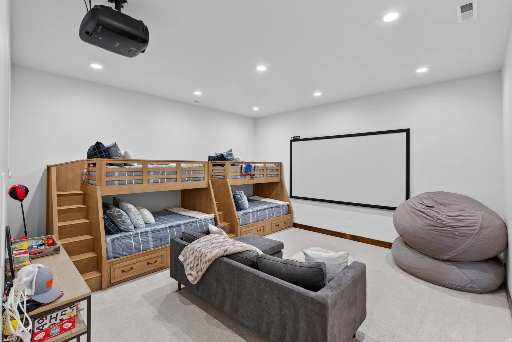 Integrated projector and screen, recessed ceiling lighting, light-toned carpeting, built-in bunk beds with storage drawers, and light wood-finish built-in steps