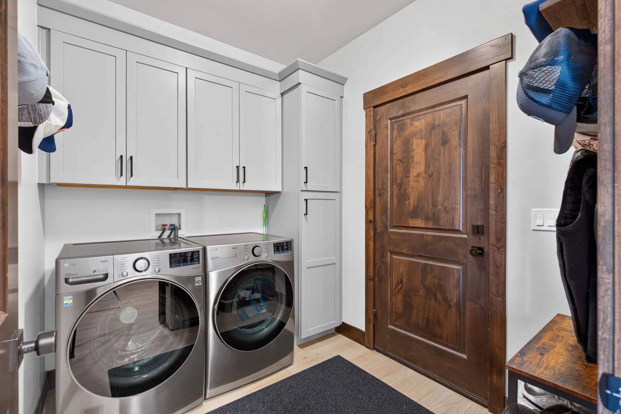 White shaker-style cabinetry with matte black hardware, wood-finish flooring, and a dark wood-paneled door
