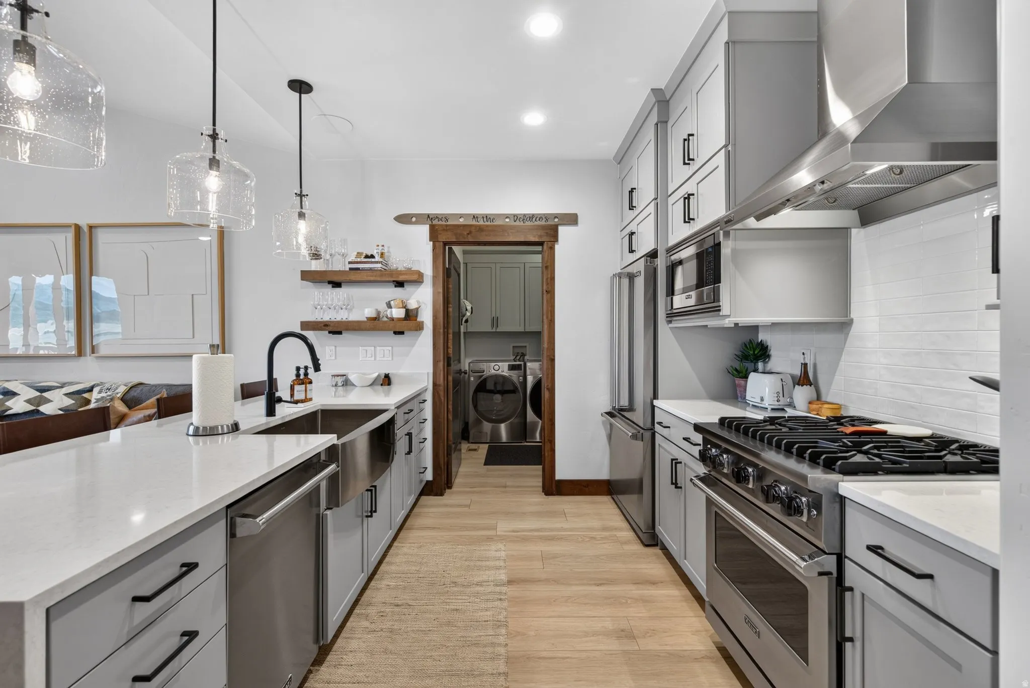 Spacious kitchen featuring an expansive island with an undermount sink, stainless steel appliances, light wood-finish flooring, recessed lighting, and a barn door entry