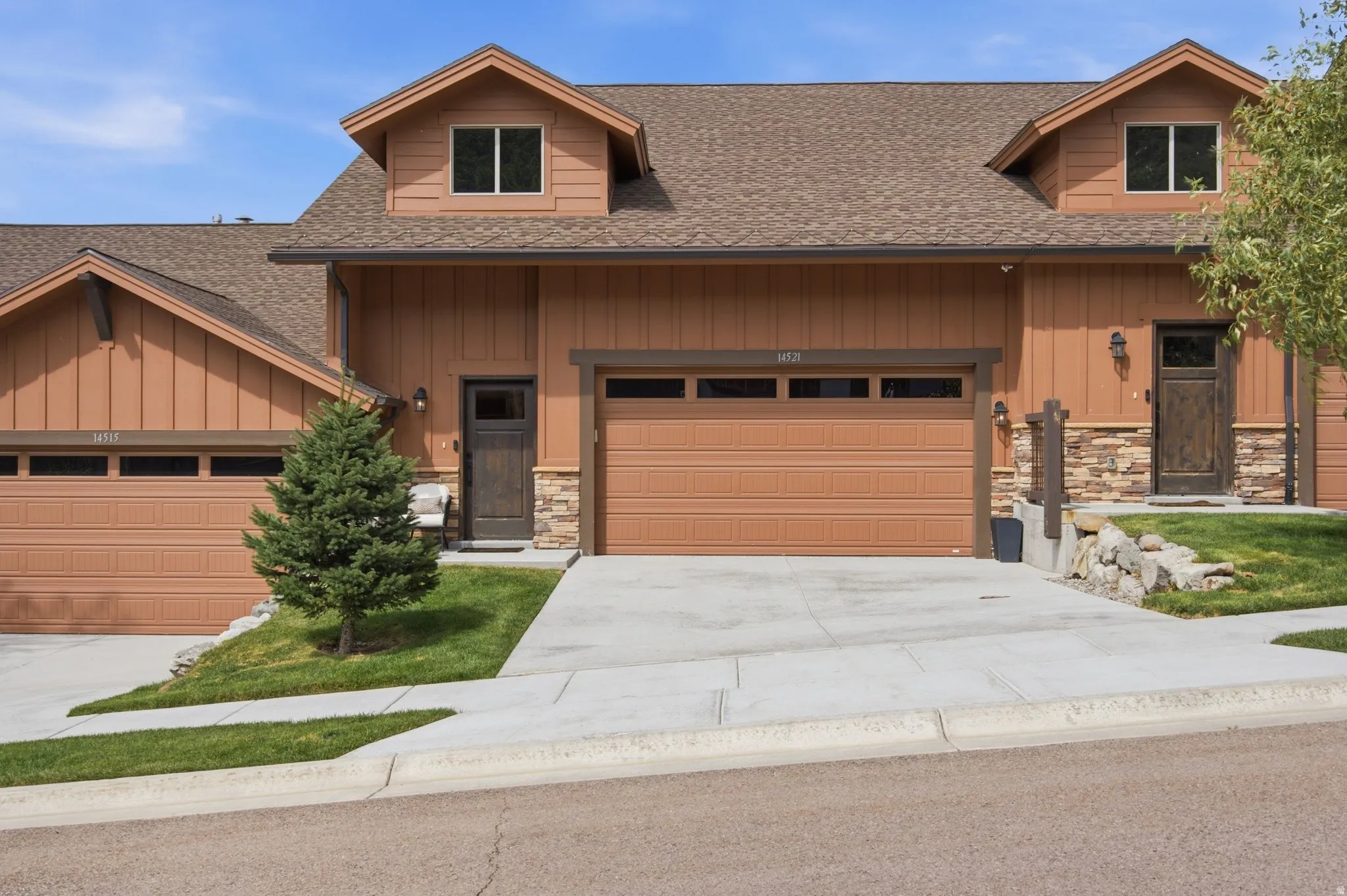 Exterior featuring dormer windows, natural wood-tone siding, stone accents, and an attached garage with panel detailing