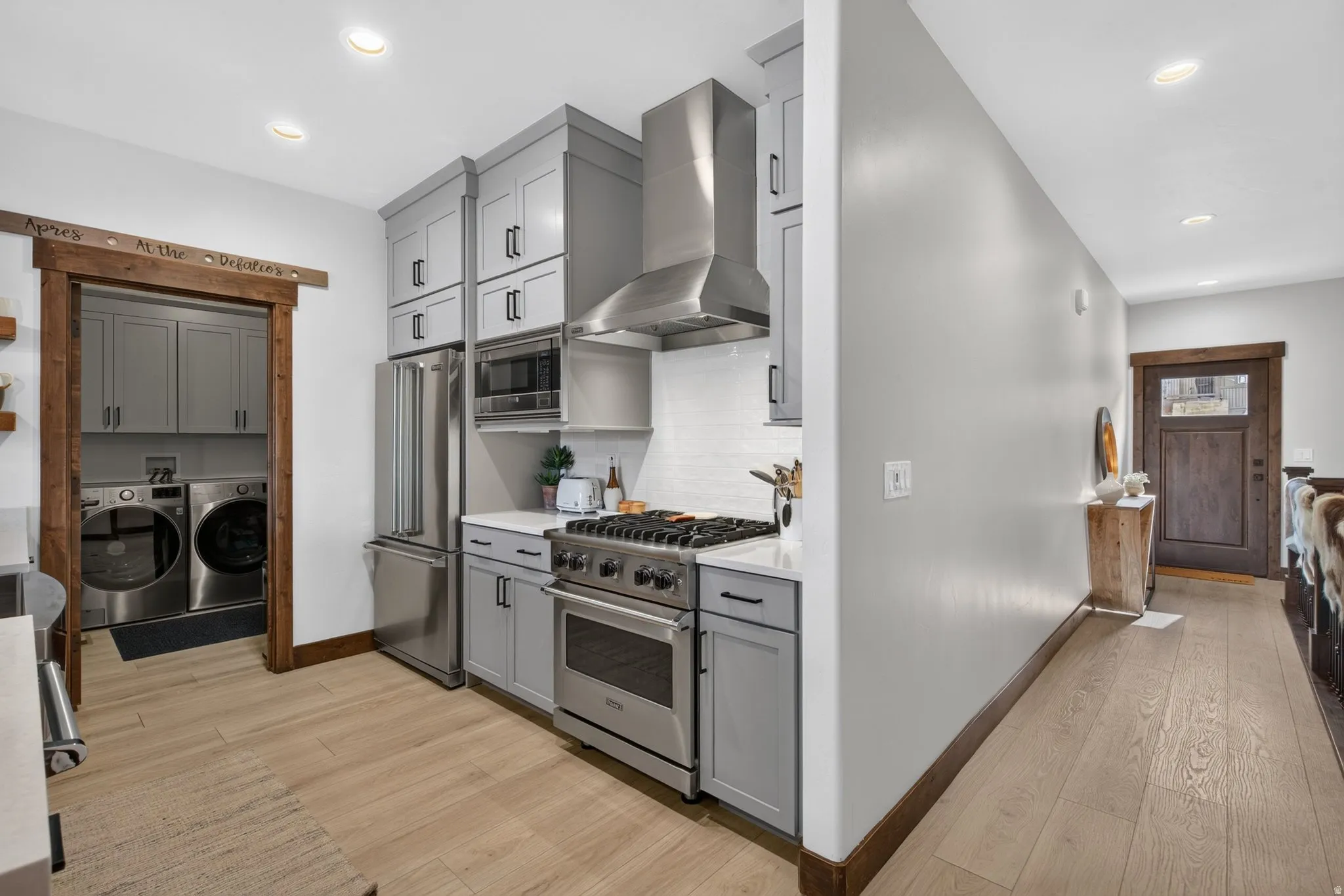 Stainless steel appliance suite, gas range with professional hood, light-toned wood-finish flooring, recessed lighting, and a built-in stacked laundry center