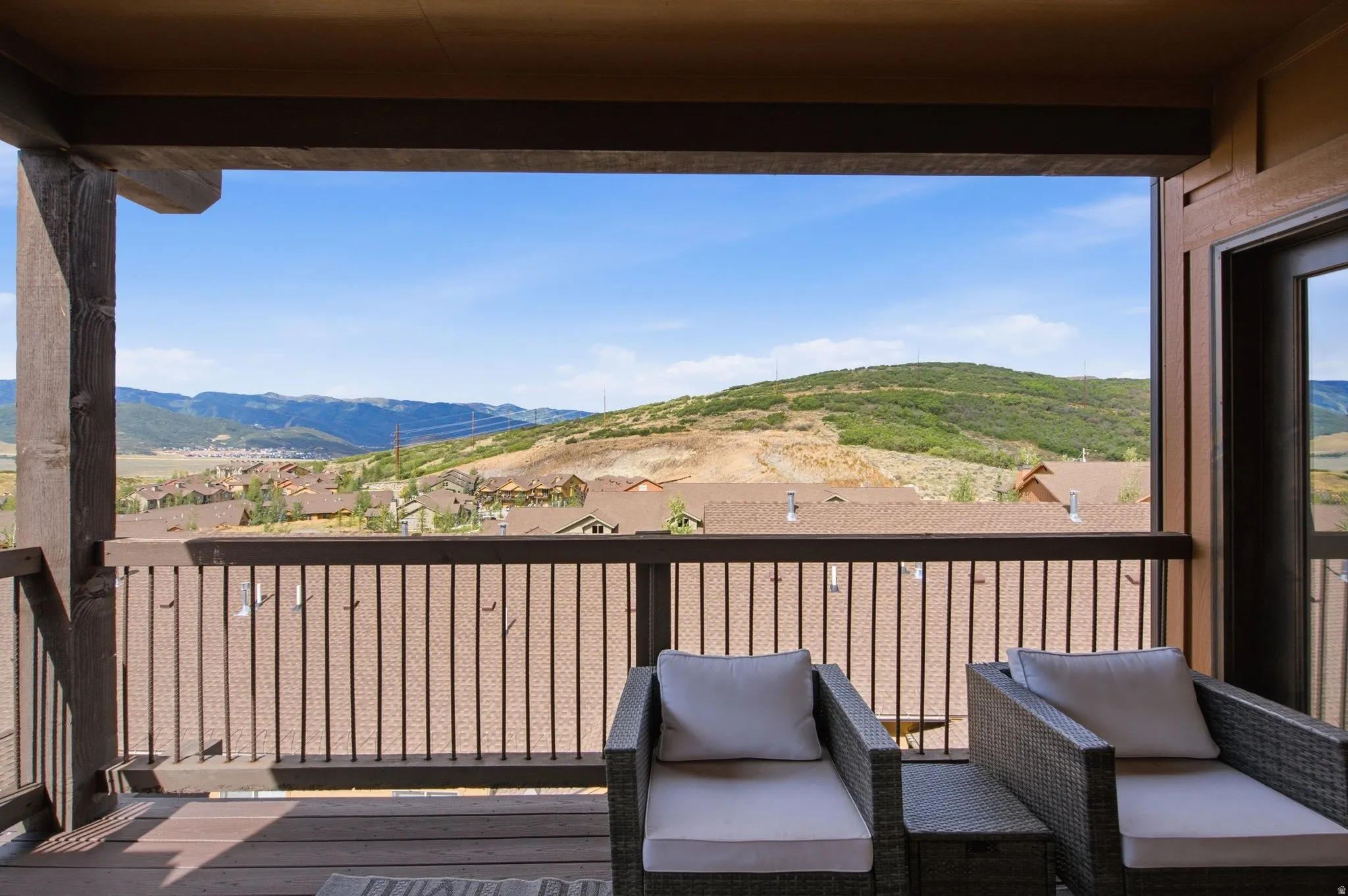 Covered balcony with wood-finish decking, dark metal railing, and exposed structural beams